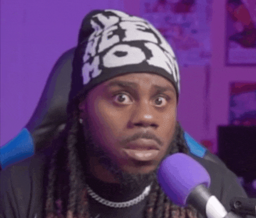a man with dreadlocks and a beanie is sitting in front of a microphone and making a funny face .