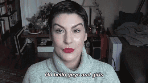 a woman with short hair is wearing a sweater and red lipstick and is talking to the camera .