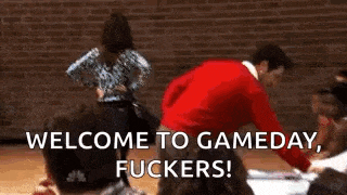 a man in a red sweater is standing in front of a group of people and says welcome to gameday , fuckers