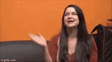 a woman with long black hair is sitting on a couch with her hands outstretched .