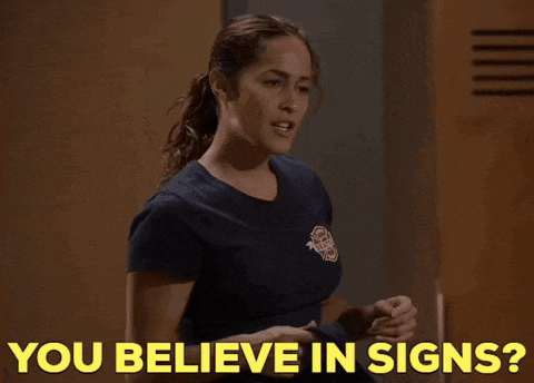 a woman in a blue shirt is pointing at herself and says " you believe in signs "