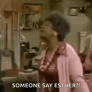 a woman in a pink coat is standing in a living room and talking to someone .