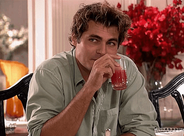 a man in a green shirt is drinking a glass of juice