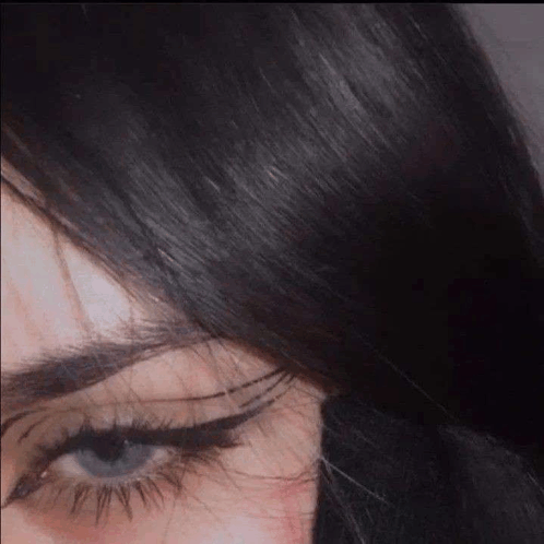 a close up of a woman 's face with long black hair and blue eyes with eyeliner .