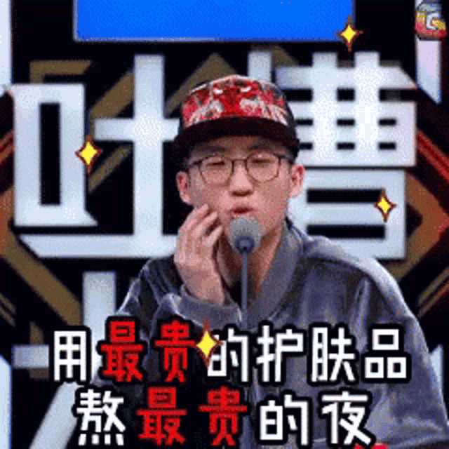 a man wearing glasses and a hat is talking into a microphone with chinese writing behind him