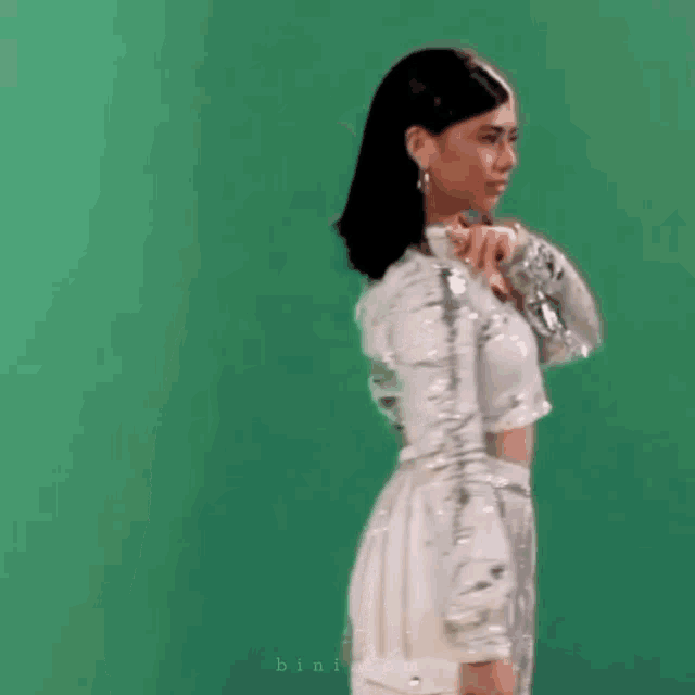 a woman is standing in front of a green screen wearing a silver dress .