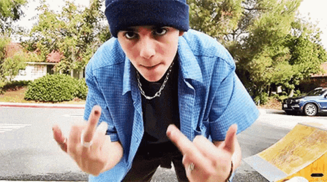 a young man wearing a blue shirt and a blue beanie giving the middle finger