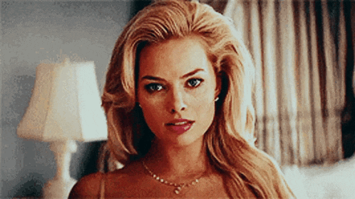 a woman with blonde hair and a necklace is looking at the camera .
