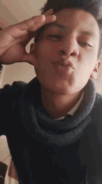 a young man wearing a sweater and tie is blowing a kiss at the camera