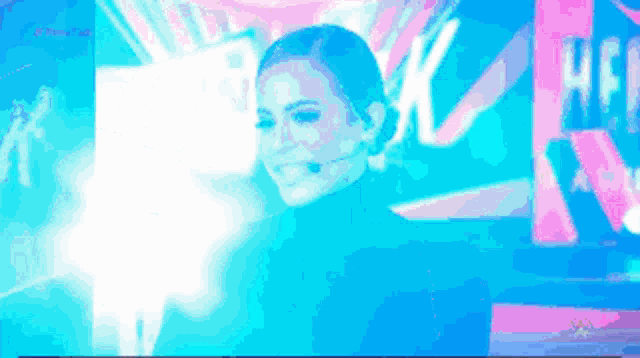 a woman with a microphone on her head is smiling in front of a blue and pink background