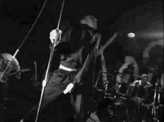 a black and white photo of a man playing a guitar and singing into a microphone on stage .