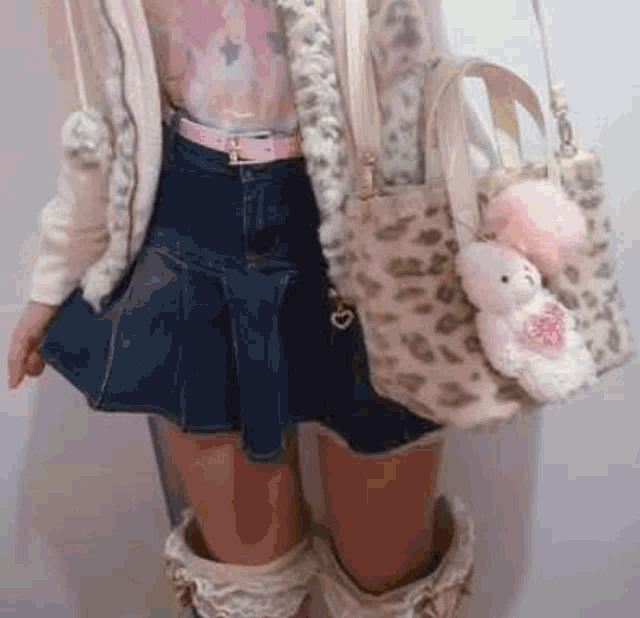 a woman is wearing a denim skirt , boots , a leopard print bag and a teddy bear .