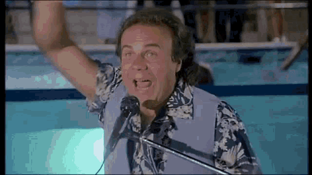 a man is singing into a microphone while standing next to a pool .