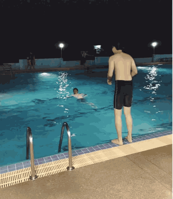 a man stands on the edge of a swimming pool watching another man swim