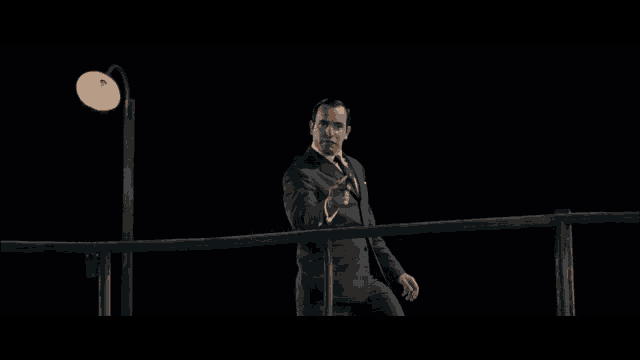 a man in a suit and tie is standing on a railing pointing