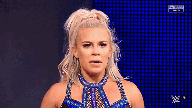 a woman in a wrestling outfit is standing in front of a blue screen .