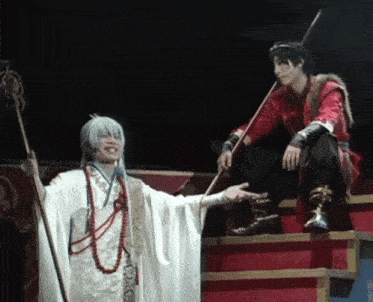 a man in a red robe is sitting on a staircase next to a man in a white robe holding a cane