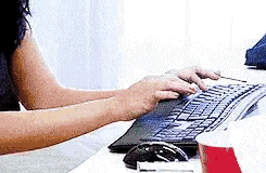 a woman is typing on a keyboard next to a cup of coffee .