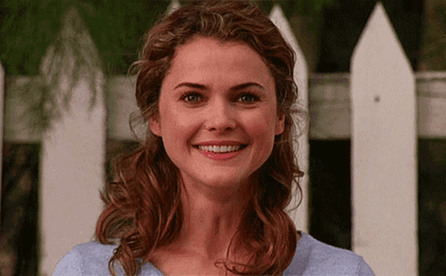 a woman smiles in front of a white fence