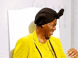 a woman in a yellow jacket and black hat is sitting in front of a mirror and smiling .