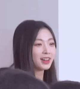 a woman with long hair is smiling and looking at the camera while sitting in front of a group of people .