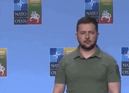 a man with a beard is standing in front of a blue wall with logos for nato .