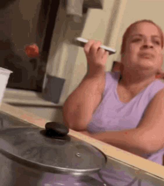 a woman in a purple tank top is sitting at a counter holding a spoon .