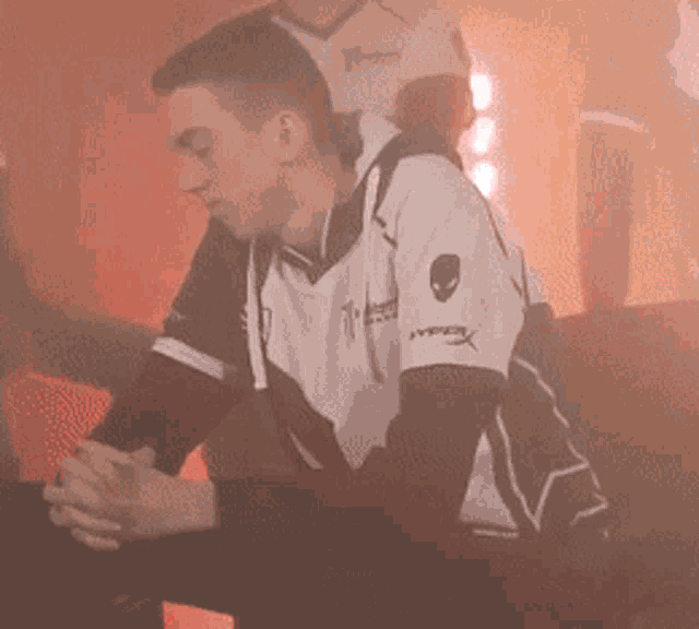 a man wearing a hyperx shirt sits on a couch with his hands folded
