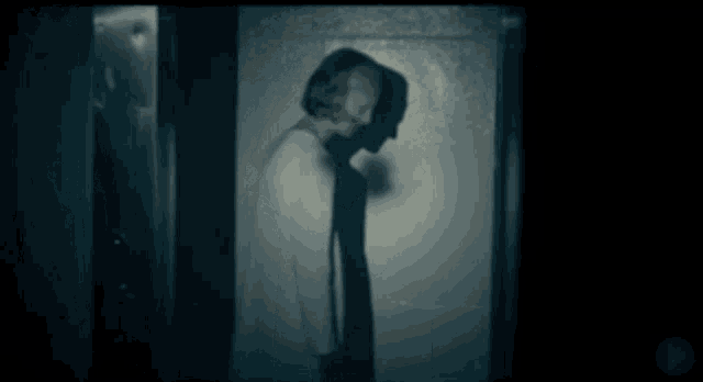 a man in a white shirt is standing in a dark room with his shadow on the wall