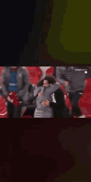 a group of people are sitting in a stadium watching a soccer game and one of them is hugging another man .