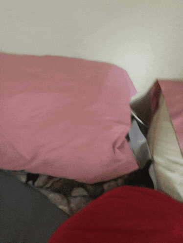a pink pillow is laying on a bed with other pillows