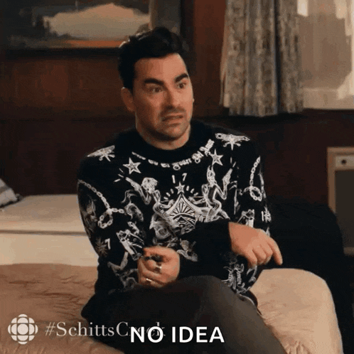 a man in a black and white sweater is sitting on a bed with the words schittsc no idea behind him