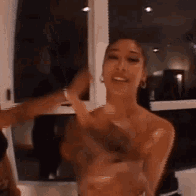 a woman without a shirt is standing in front of a window and dancing .