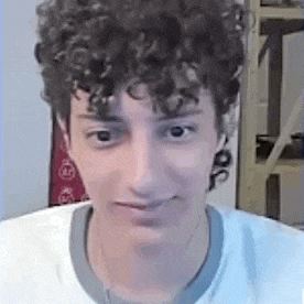 a man with curly hair is wearing a white shirt and looking at the camera .