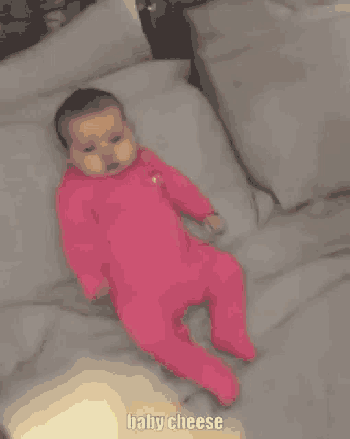 a baby in a pink outfit is laying on a bed with a pillow .