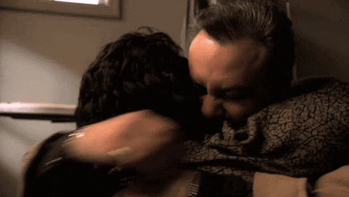 a man is kissing another man on the cheek in a dark room