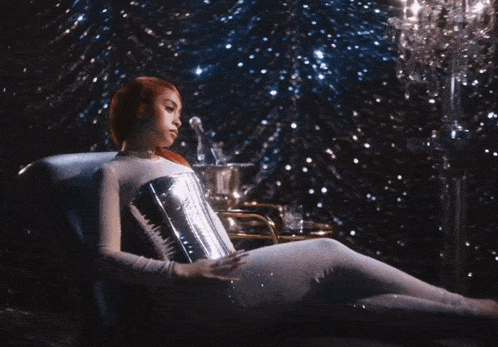 a woman with red hair is sitting in a chair with a bottle of champagne in the background