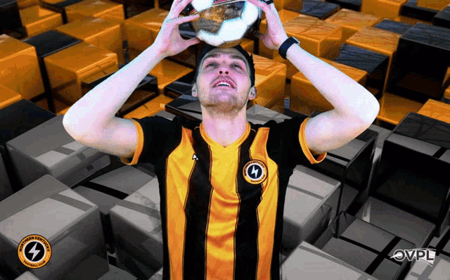 a man wearing a black and yellow striped shirt holds a soccer ball in his hands