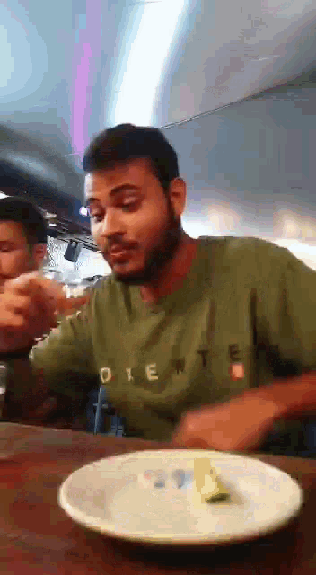 a man wearing a green shirt that says oriente is sitting at a table with a plate of food in front of him