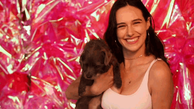 a woman in a white tank top is holding a puppy and smiling