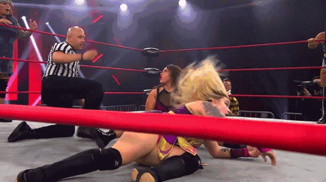 a woman is laying on the ground in a wrestling ring with a referee