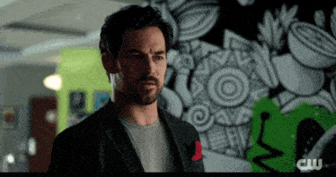 a man with a beard is standing in front of a wall with a cw logo