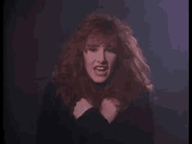 a woman with red hair is wearing a black dress and dancing in a dark room .