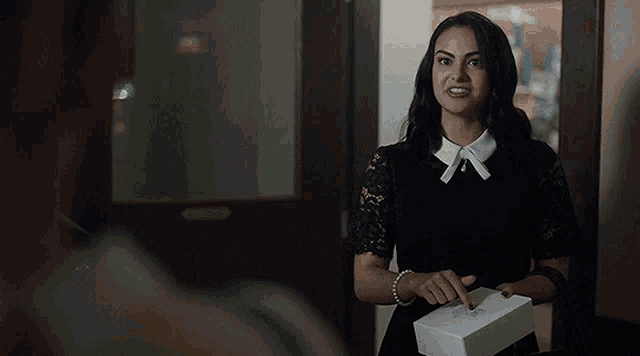 a woman in a black dress and white collar is holding a white box