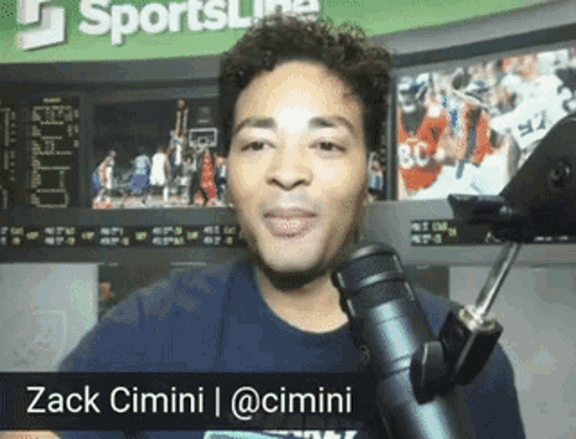 a man stands in front of a microphone with the name zack cimini at the bottom