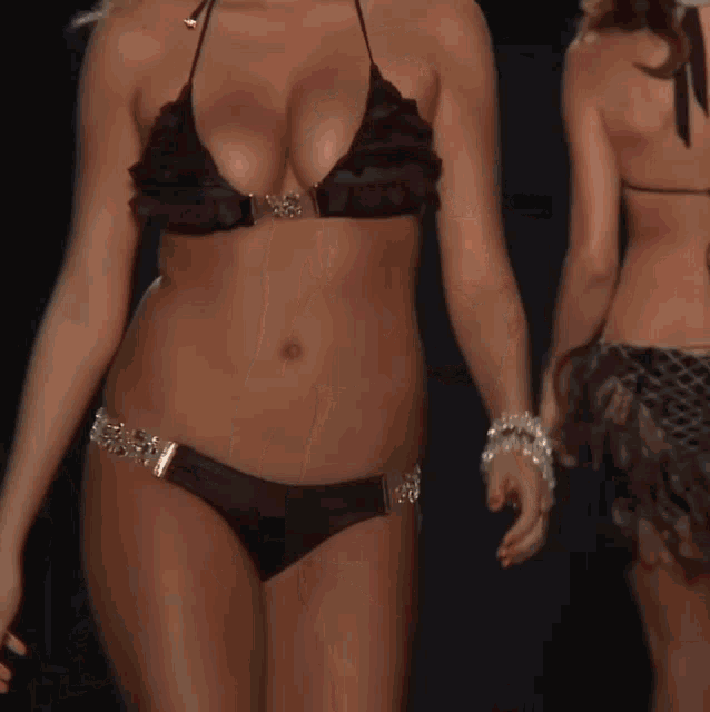 a woman in a black bikini with ruffles on the top is walking down a runway