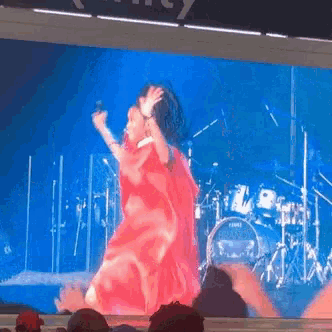 a woman in a red dress is dancing on stage in front of a drum set that says yamaha