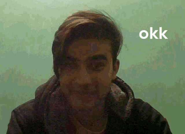 a man 's face is shown in front of a green wall and the word okk is visible
