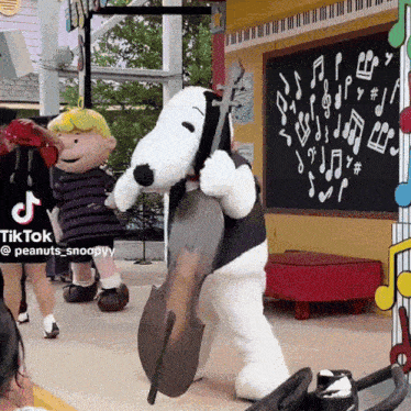 a snoopy mascot is playing a double bass in front of a chalkboard with music notes on it
