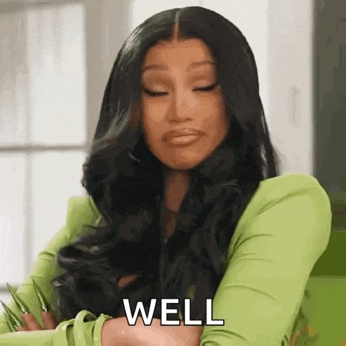 a woman with long black hair is wearing a green shirt and says well